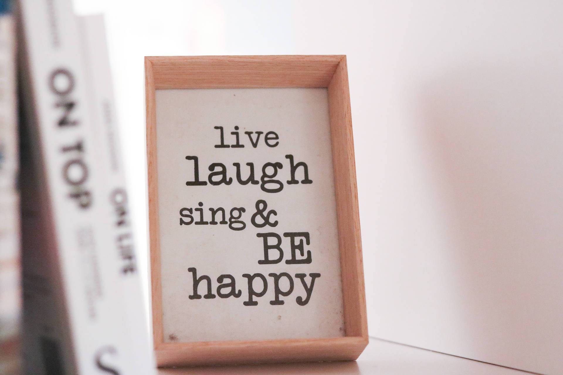 木框勵志語錄標牌，寫著 live laugh sing & BE happy，旁邊有書本。