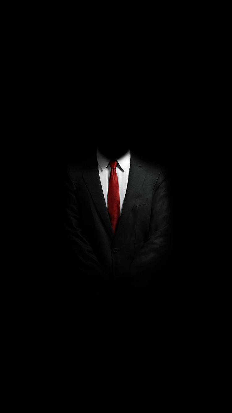 極簡風格《殺手》iPhone壁紙 壁紙 — 一個身穿黑色西裝和紅色領帶的人物，在完全黑暗中站立，沒有可見的臉孔，營造出詭異而神秘的氛圍。