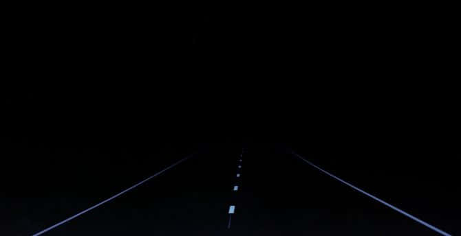 夜晚的黑暗道路，發光的白色車道標線延伸至遠方