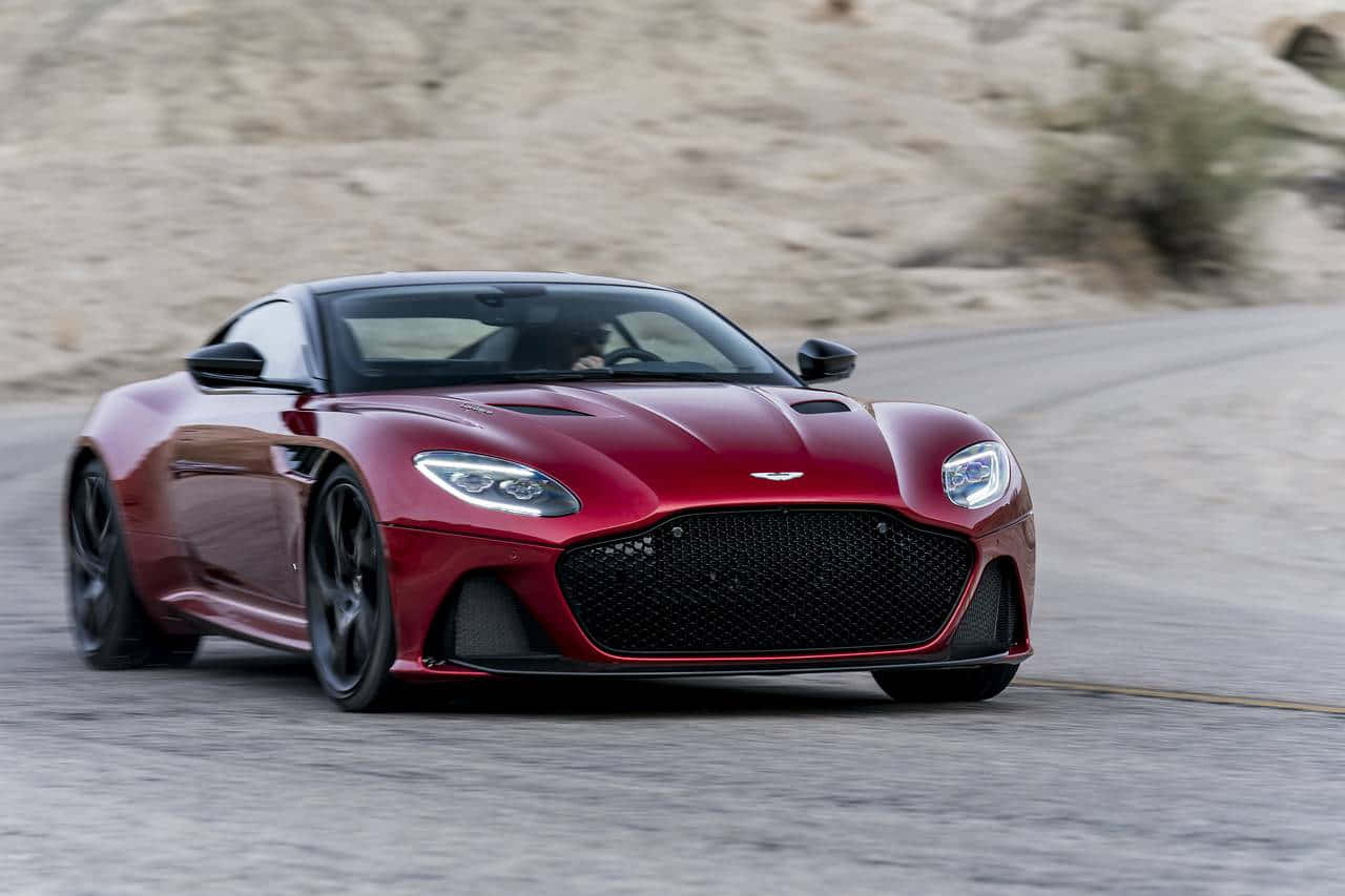 極致奢華——阿斯頓·馬丁 壁紙 — 一輛流線型的紅色Aston Martin跑車在蜿蜒的沙漠公路上疾馳，帶有模糊的動感。