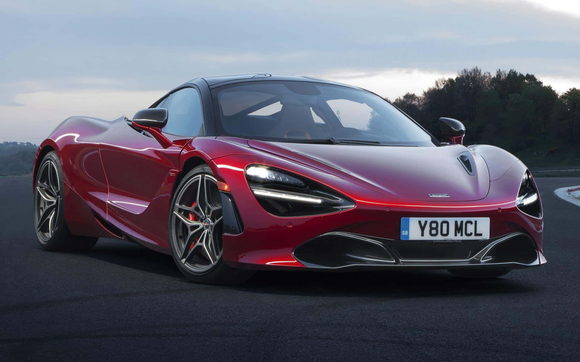 紅色McLaren 720S跑車在賽道上，背景有樹木和多雲的天空。