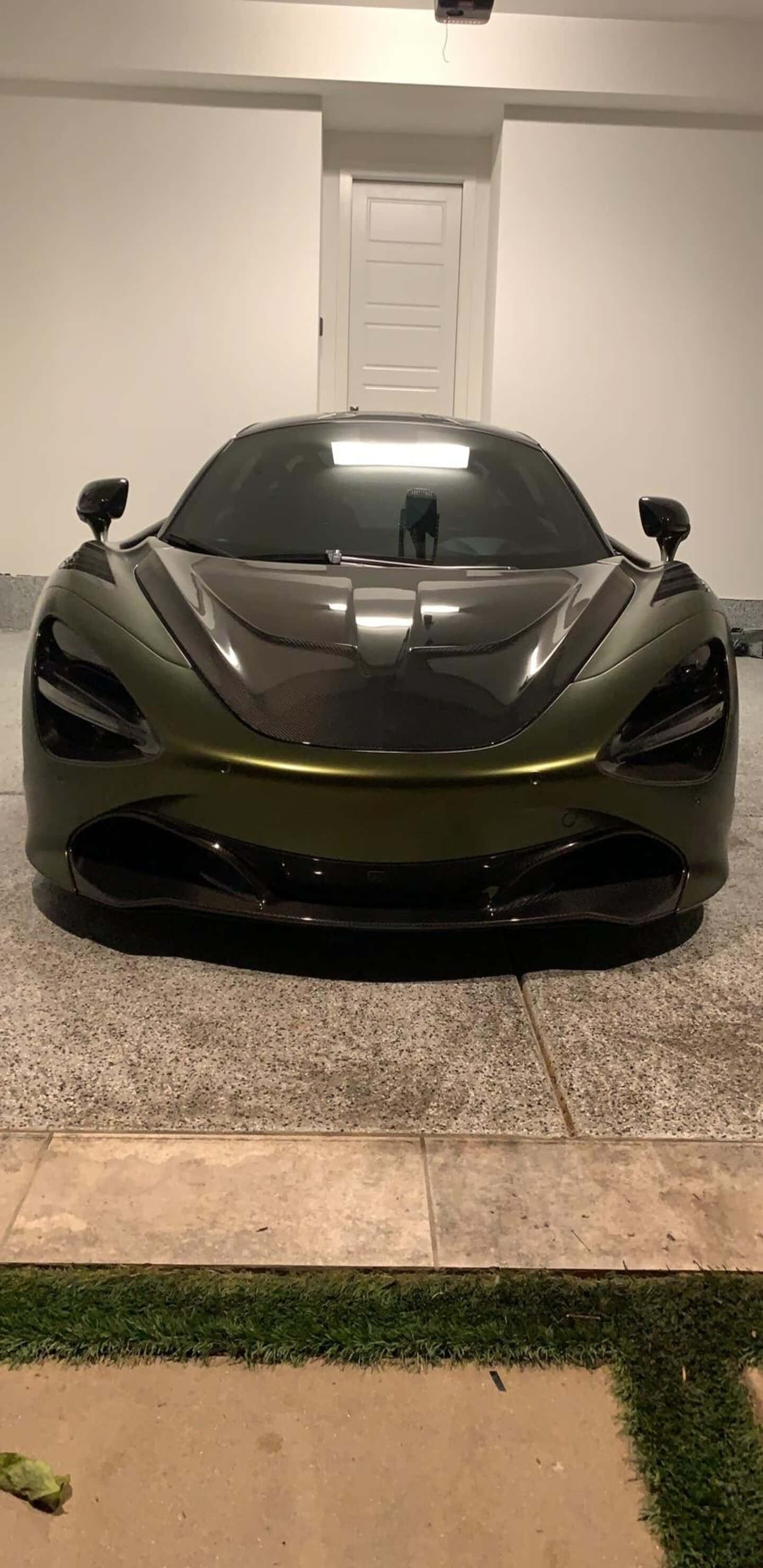 極致炫酷麥拉倫720S Pixel 3XL 壁紙 — 一架光滑的啞光橄欖綠色McLaren跑車停放在室內瓷磚地板上，帶有人造草邊界。