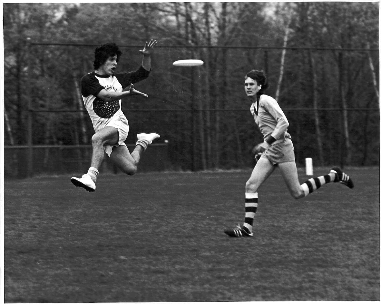 極致腎上腺素：Ultimate Frisbee 動作瞬間 壁紙 — 兩名運動員在黑白照片中激烈競爭，其中一人跳起接住飛行的飛盤，背景是草地。