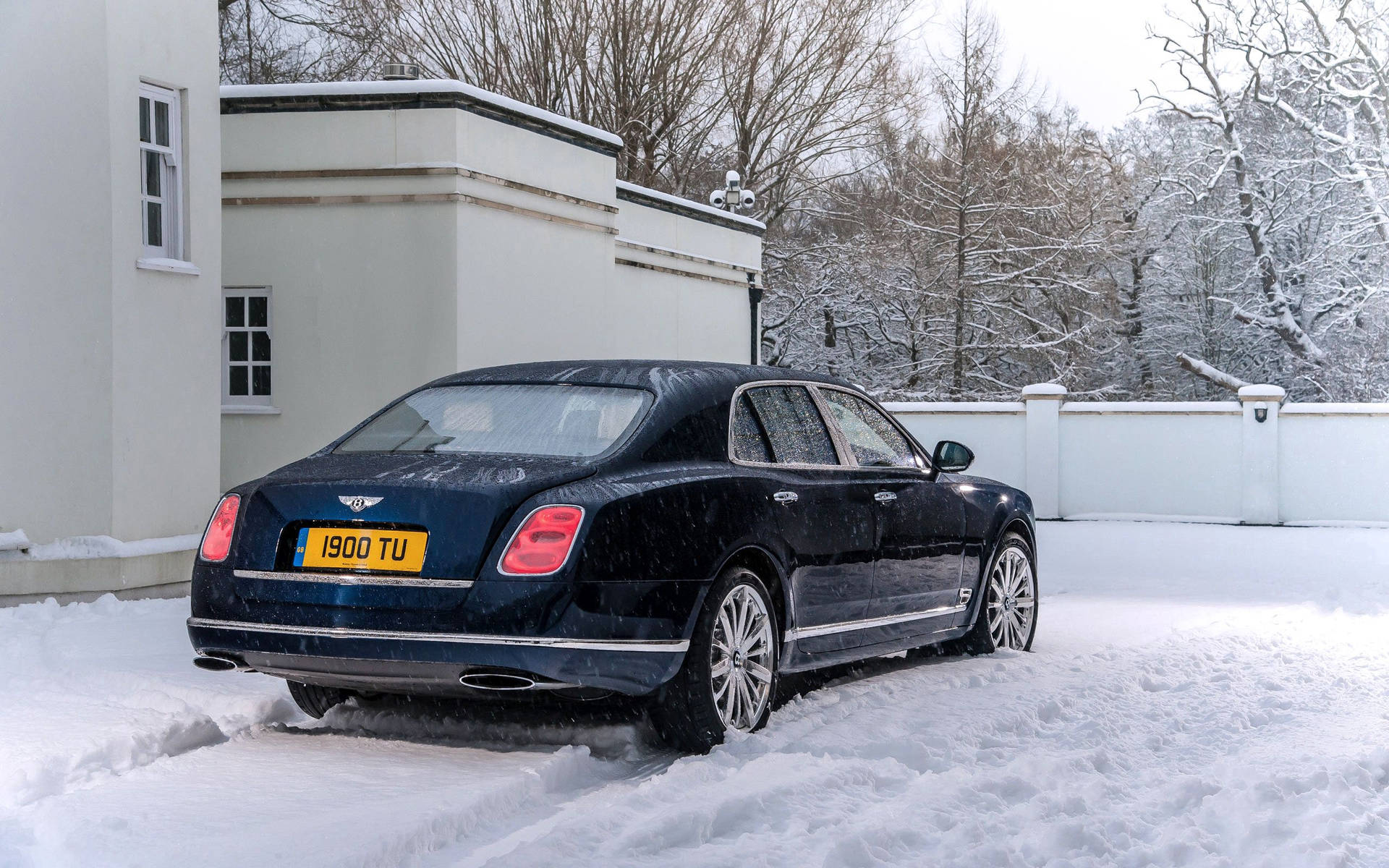黑色賓利豪華轎車停在白色房子旁邊的雪地車道上。