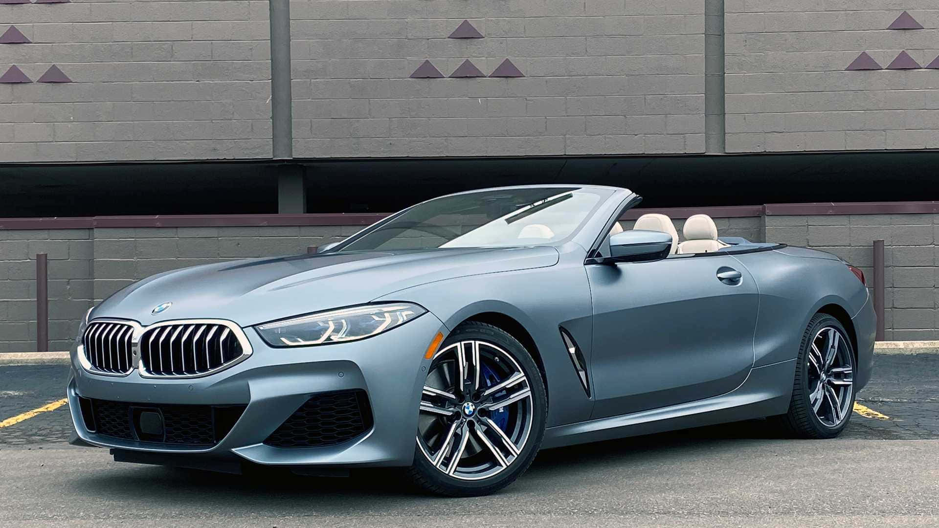 極致駕駛機 — BMW 壁紙 — 一架流線型啞光灰色寶馬開篷車停泊在帶有三角形裝飾的灰色磚牆前。