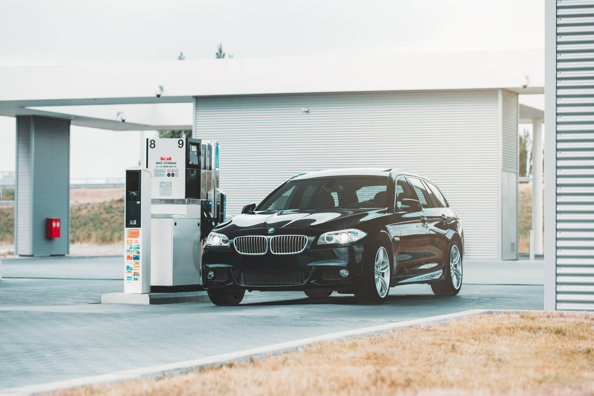 黑色BMW旅行車在現代化加油站，天空多雲。