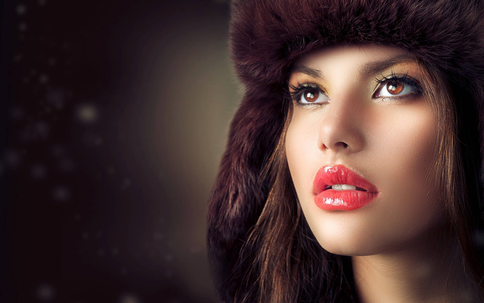 戴皮草帽、紅唇的女性在雪景中向上看。