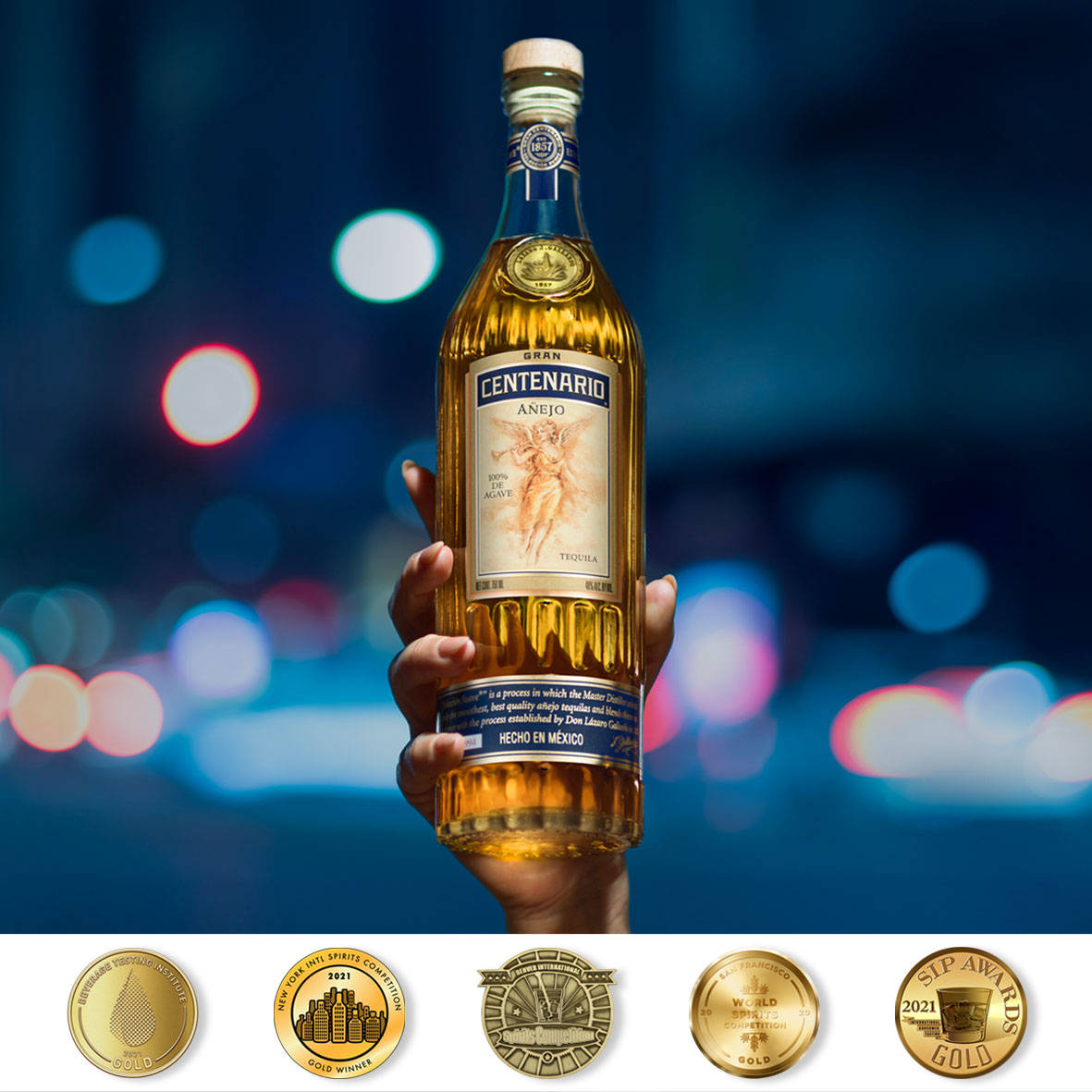 手拿著一瓶Gran Centenario Añejo龍舌蘭酒，背景有城市燈光。
