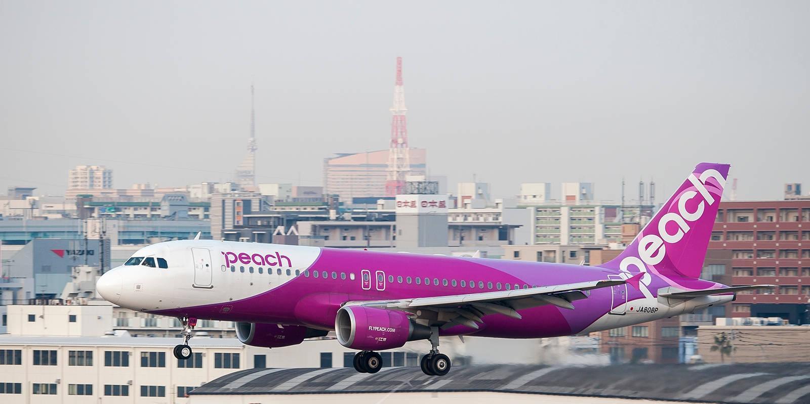 Peach Airlines飛機在城市景觀上空爬升，可見一座塔。