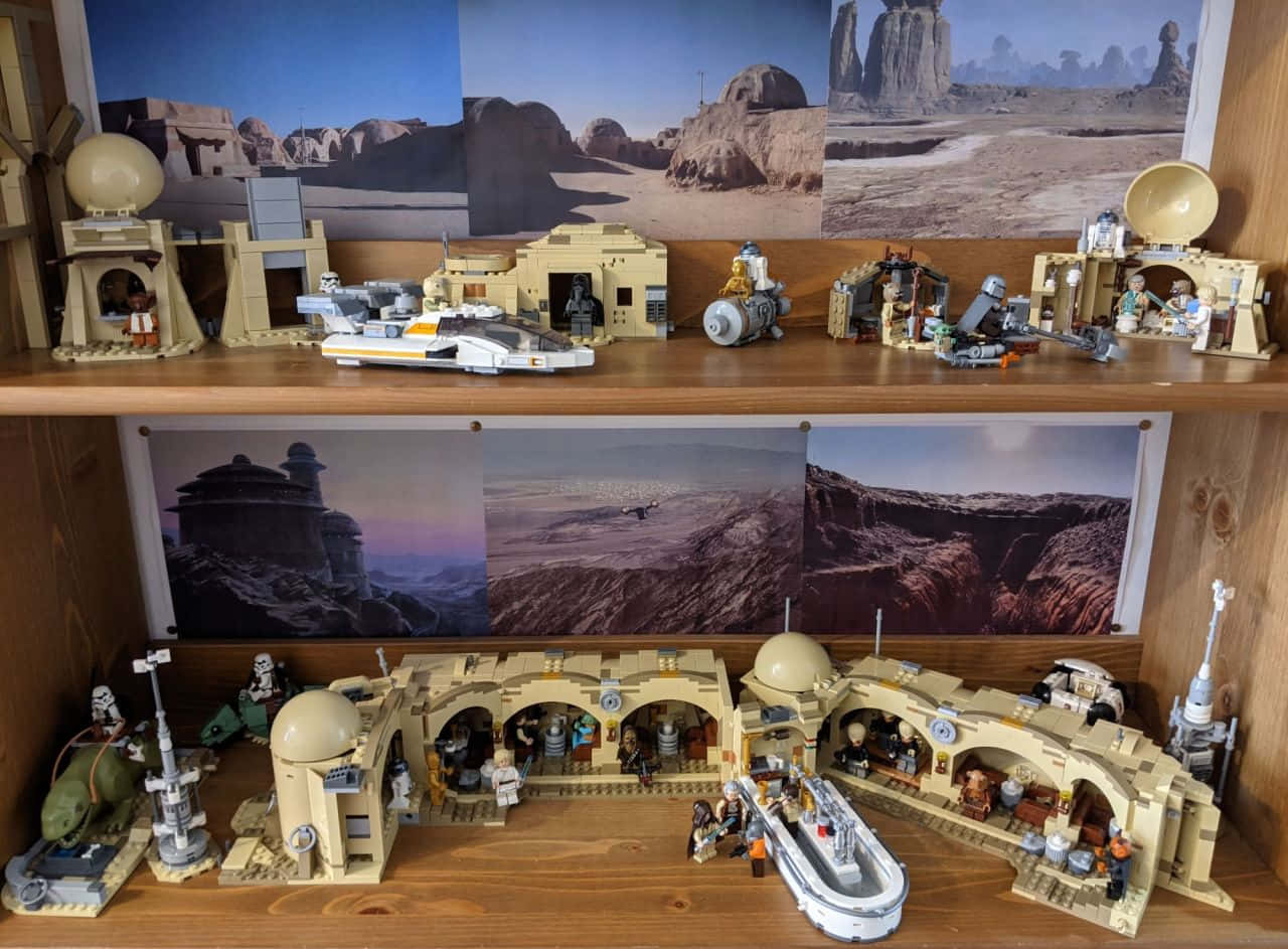 樂高塔圖因建築套件 壁紙 — 一個詳細的LEGO星際大戰塔圖因立體模型，展示在木架上，配有沙漠背景海報的沙地爬行者和飛車模型。