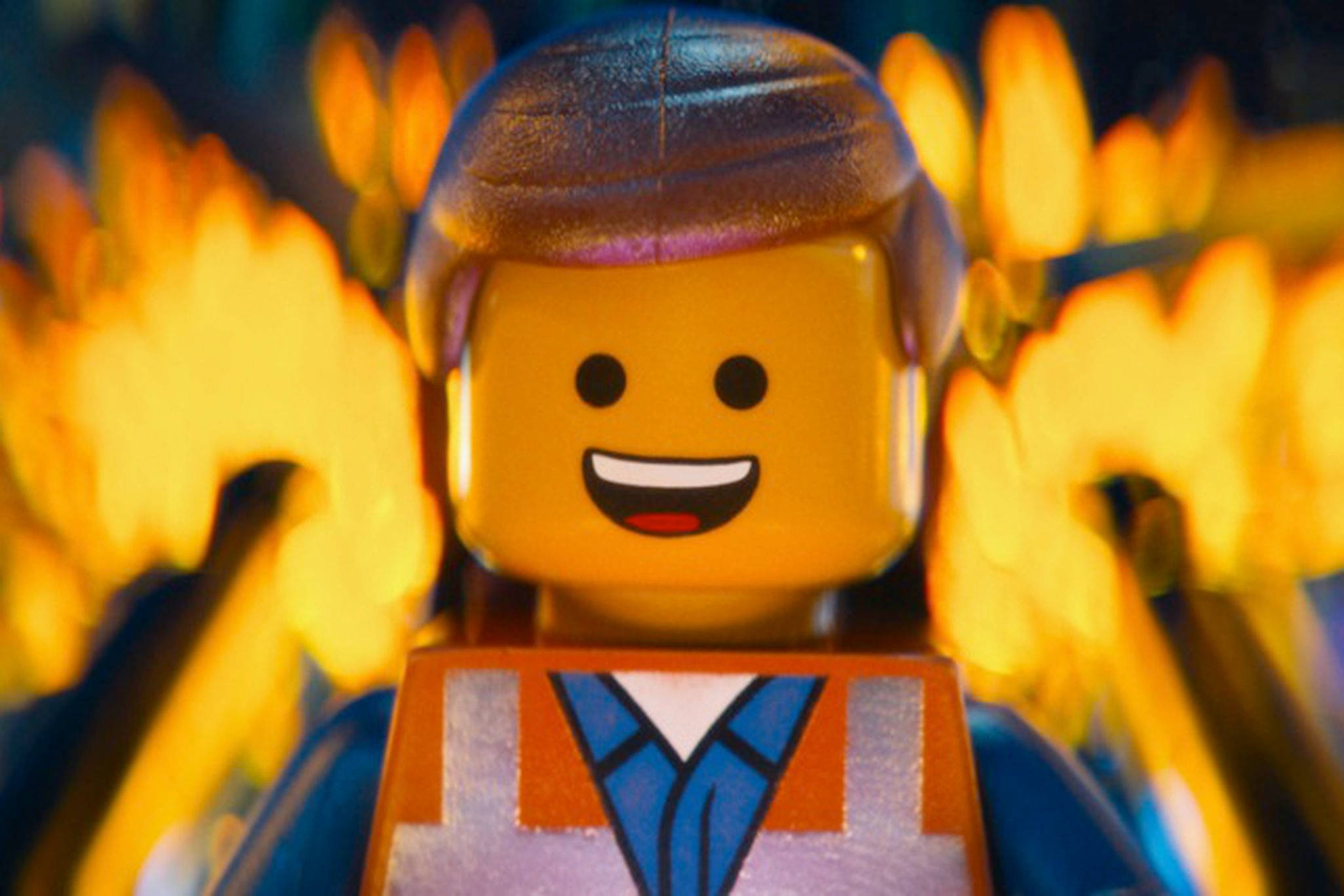 《樂高大電影》微笑艾米特 壁紙 — 微笑的LEGO人仔特寫，棕色頭髮，藍色西裝，背景是火橙色散景。
