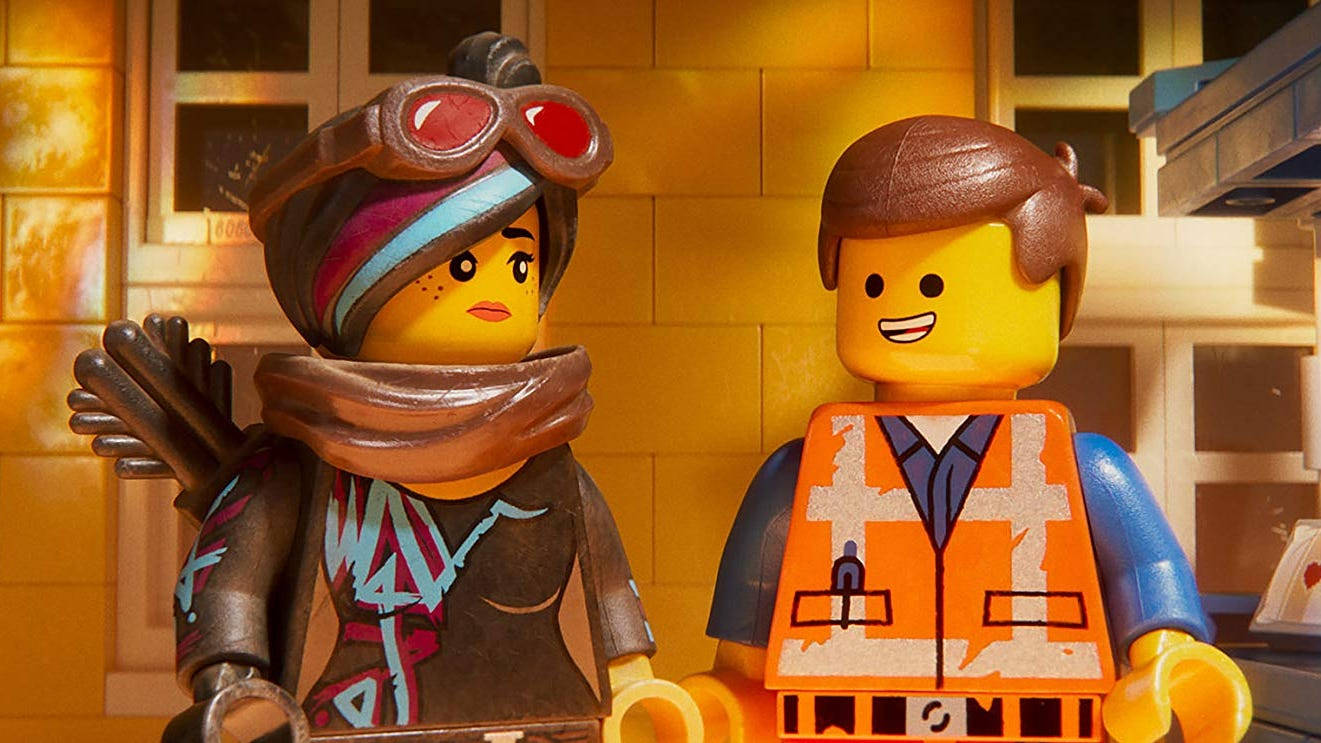 《樂高大電影》艾米特與薇樂絲泰 壁紙 — 兩個LEGO角色並排站在一個光線溫暖的室內環境中，有磚牆和窗框。