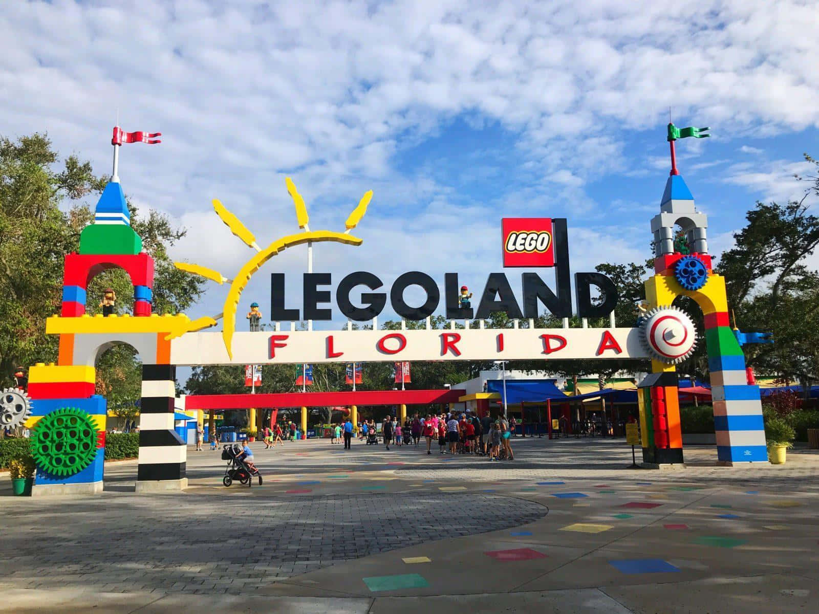 樂高樂園冒險即將開始！ 壁紙 — 色彩繽紛的LEGO主題入口拱門，設有彩色積木塔和微笑的太陽，天空部分多雲。