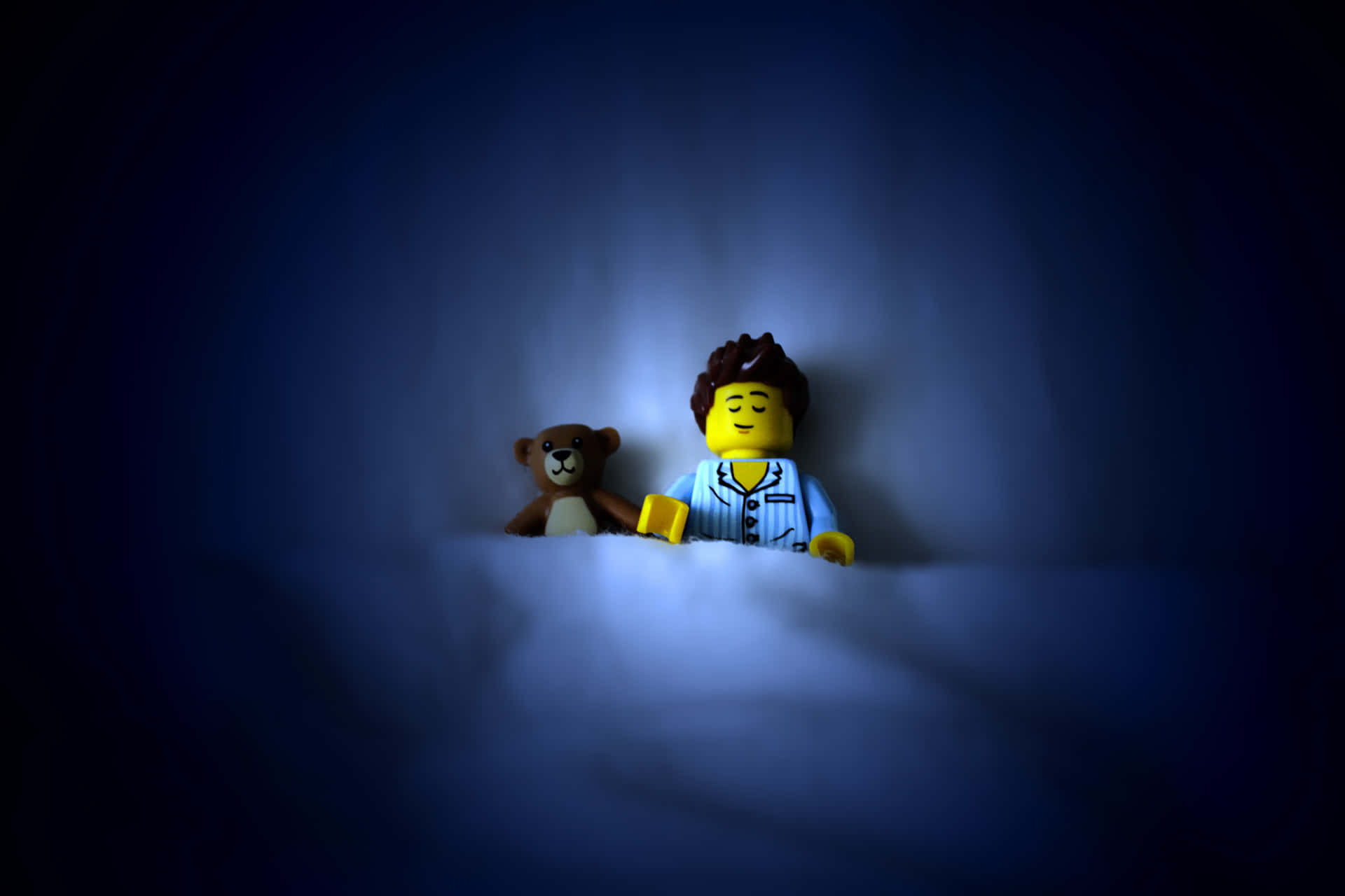 穿著睡衣的LEGO人偶在藍光下在泰迪熊旁邊睡覺。