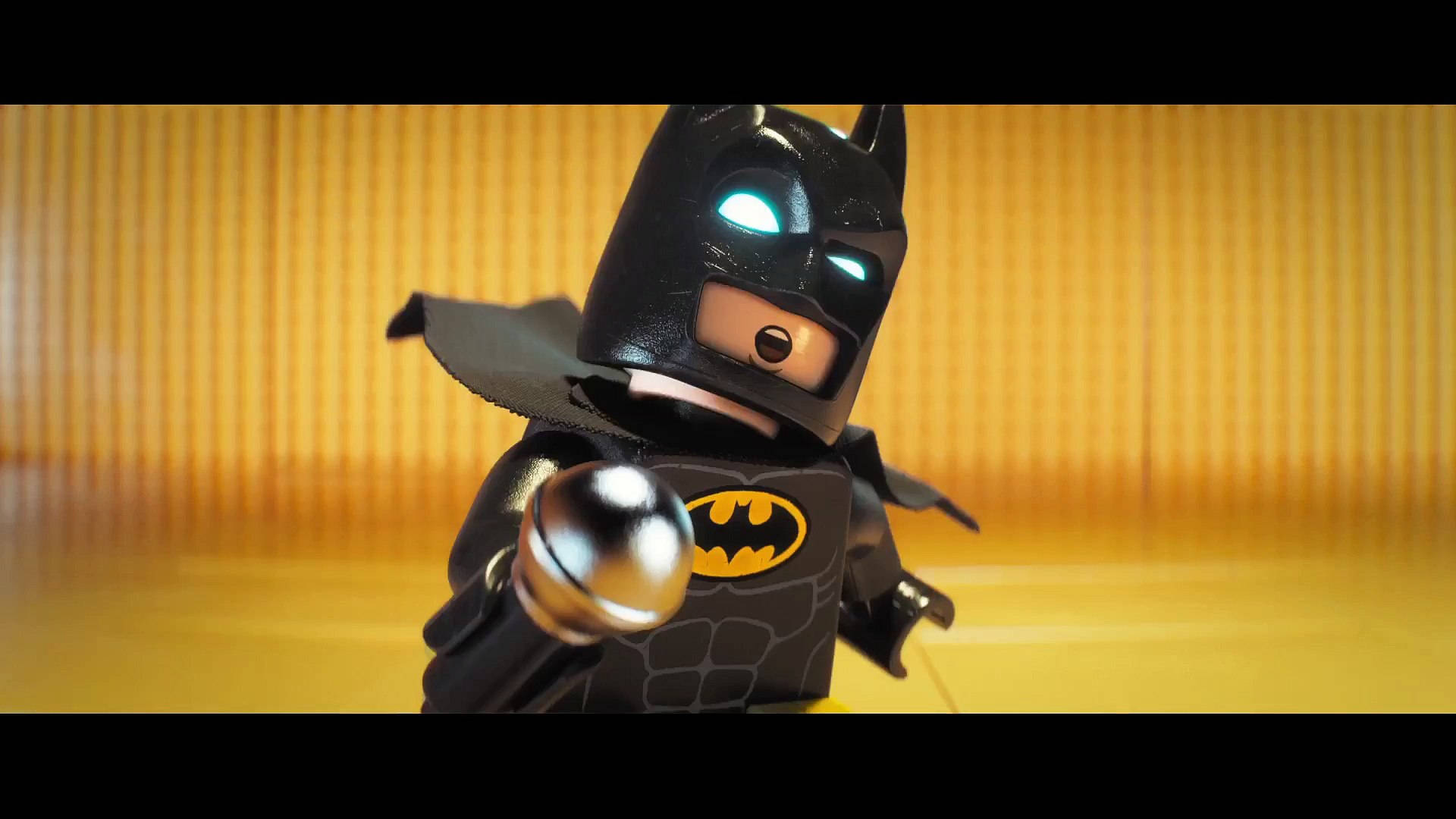 樂高蝙蝠俠電影中的小蝙蝠俠 壁紙 — LEGO Batman 迷你人偶特寫，擁有發光的藍色眼睛和蝙蝠標誌，站在溫暖的黃色竹子背景前。