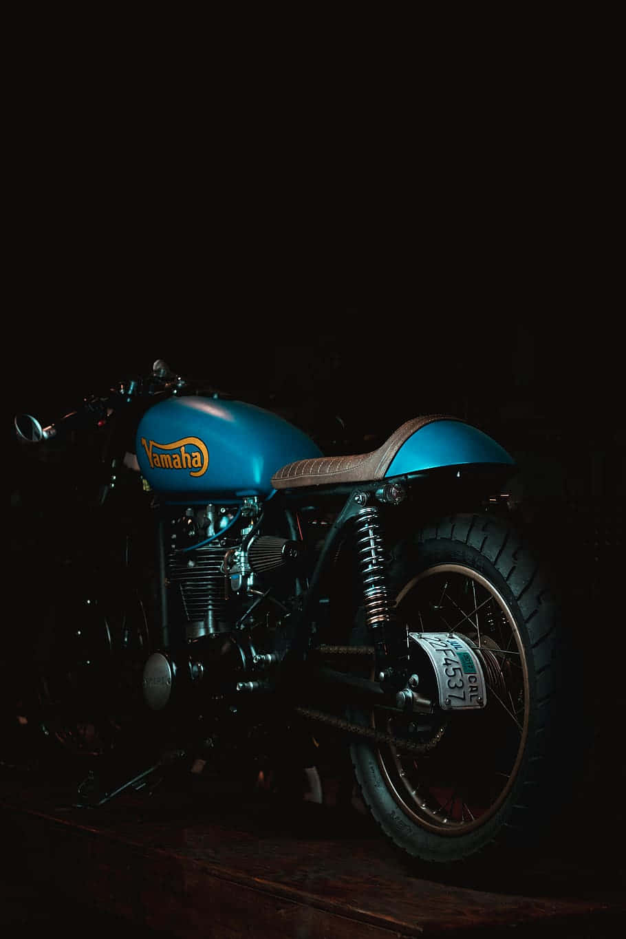 標準 Royal Enfield Thunderbird 壁紙 — 一輛復古藍色Yamaha電單車，配備棕色皮革座椅，在黑色背景上戲劇性地照亮。