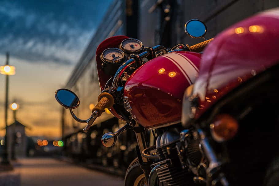 標準Triumph Thruxton壁紙 壁紙 — 一輛光澤的紅色復古電單車在暮色街燈下閃耀，背景有散景燈光。