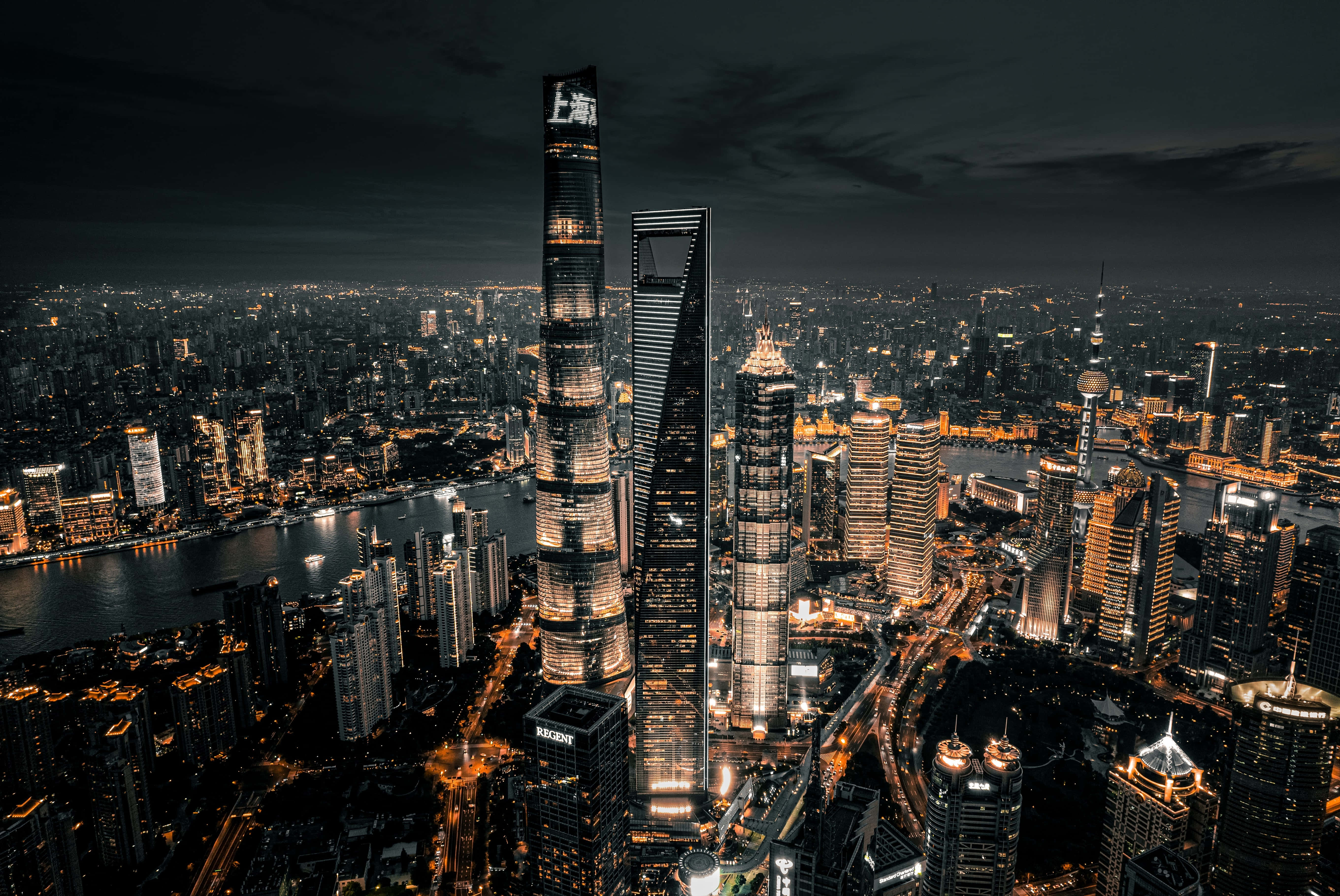 標準城市夜景鳥瞰圖 壁紙 — 上海璀璨摩天大樓與河流的夜間航拍，城市燈光在黑暗天空中閃耀。