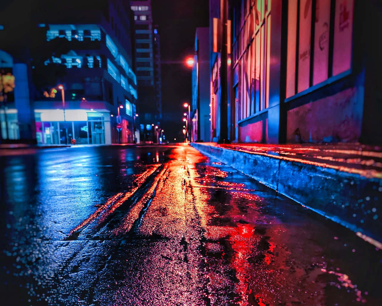 標準霓虹街景壁紙 壁紙 — 一條充滿霓虹燈的都市街道在夜晚將鮮豔的紅藍燈光反射在濕漉漉的路面上，周圍是高聳的建築物。
