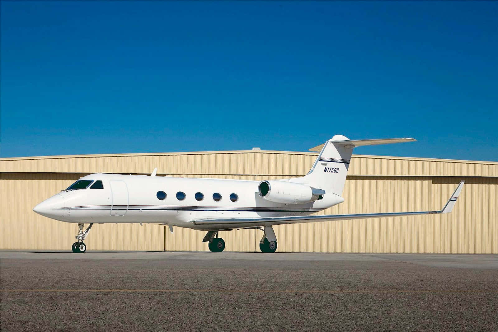 白色私人飛機停在機庫前停機坪上，藍天白雲