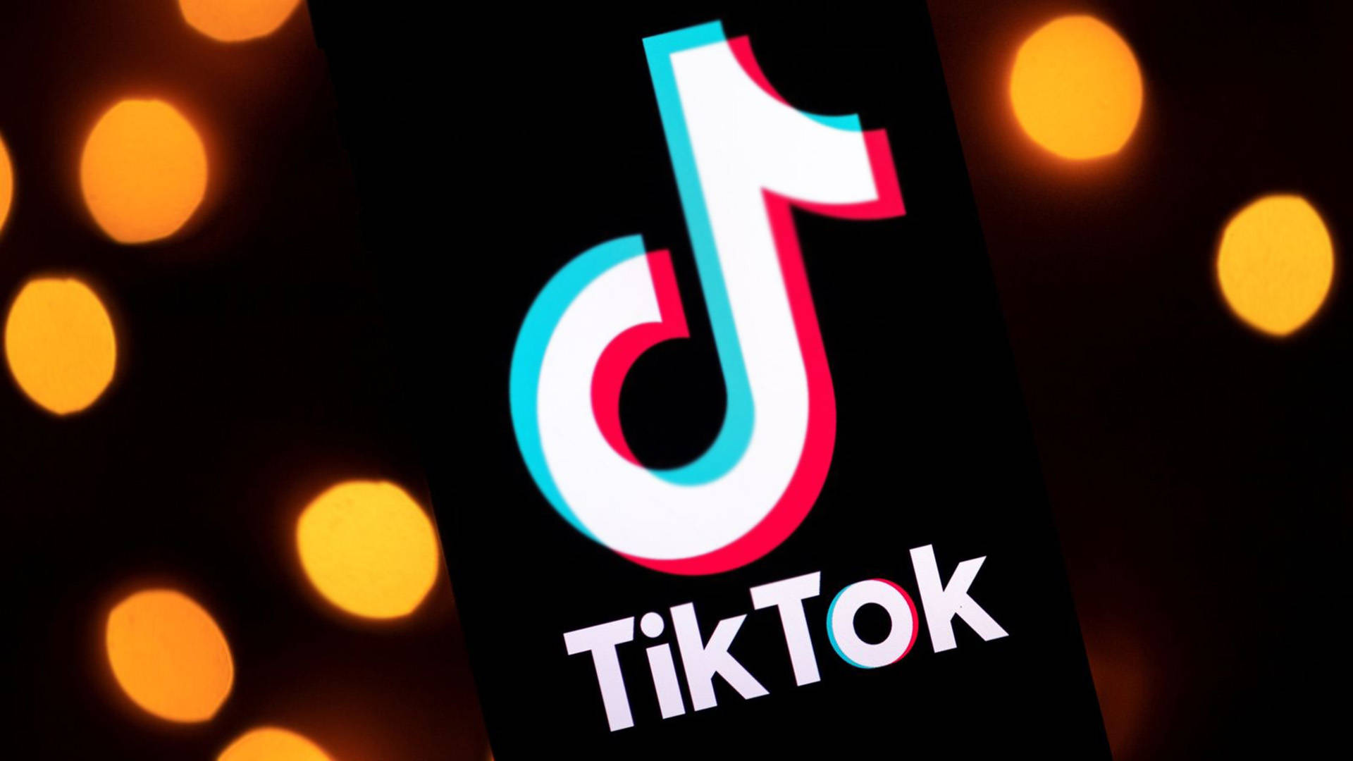 TikTok 應用程式標誌顯示在智能手機上，背景有發光的橙色燈光。