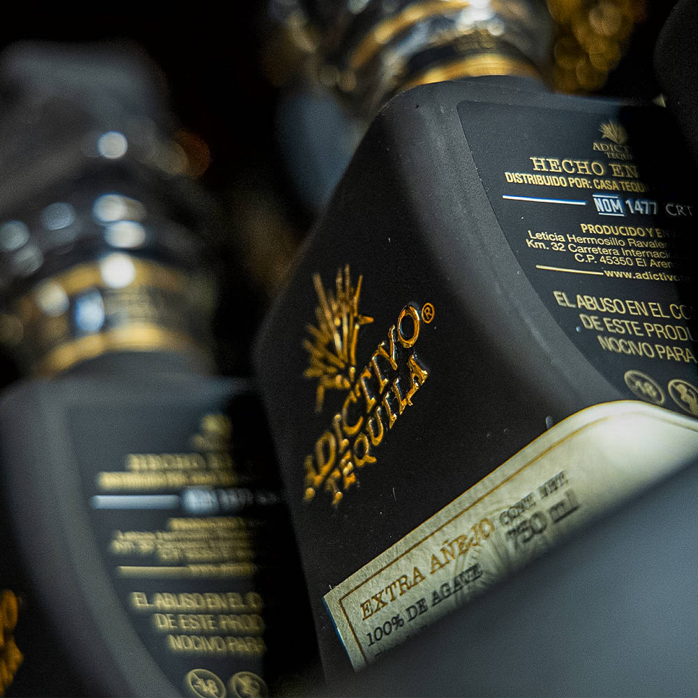 標題：Adictivo奢華黑桶陳釀龍舌蘭酒 壁紙 — 黑色龍舌蘭酒瓶特寫，帶有金色字體和標籤，顯示「Extra Añejo」和「100% de Agave」，背景為深色模糊。