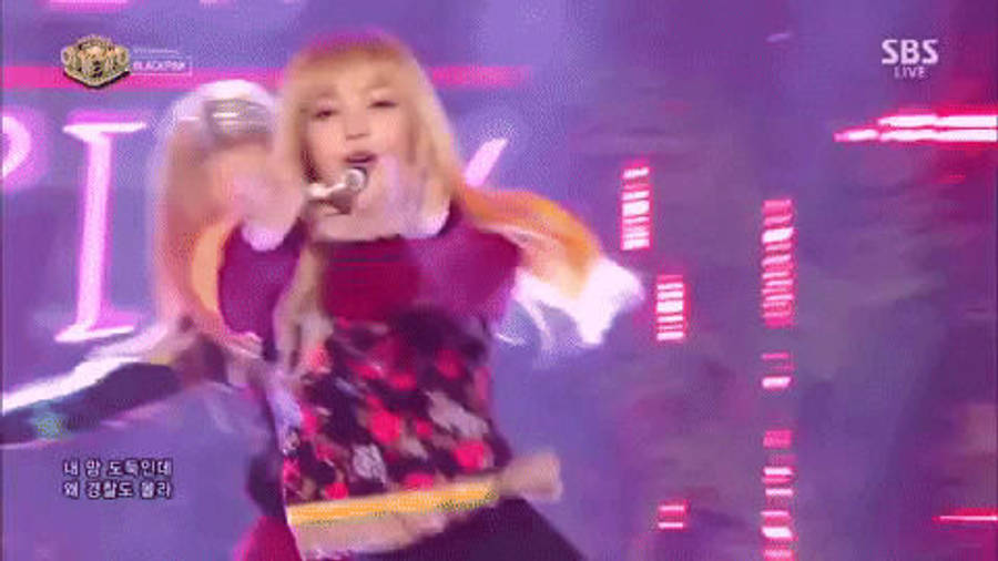 標題：BLACKPINK 梨子展現驚人舞步 壁紙 — 一位金髮歌手在充滿活力的紫色燈光舞台上，伴隨著閃爍的粉紅燈光和動態模糊效果，充滿能量地表演。