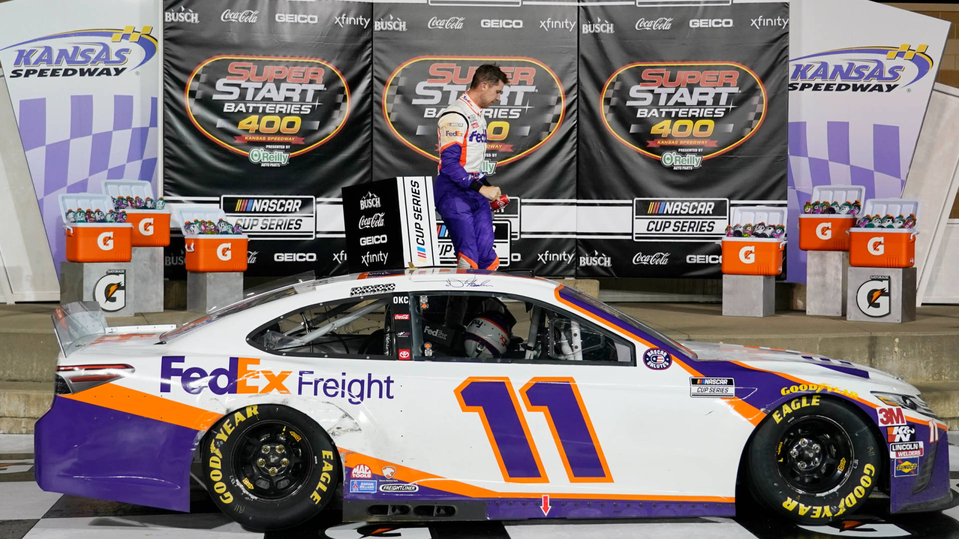 NASCAR車手在堪薩斯賽車場頒獎台上，旁邊是他的FedEx Freight賽車。