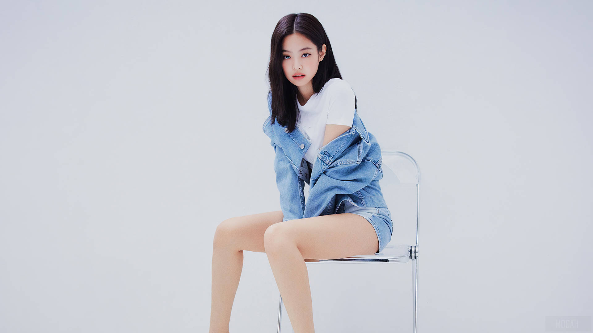 年輕女性身穿牛仔裝束坐在透明椅子上於攝影棚