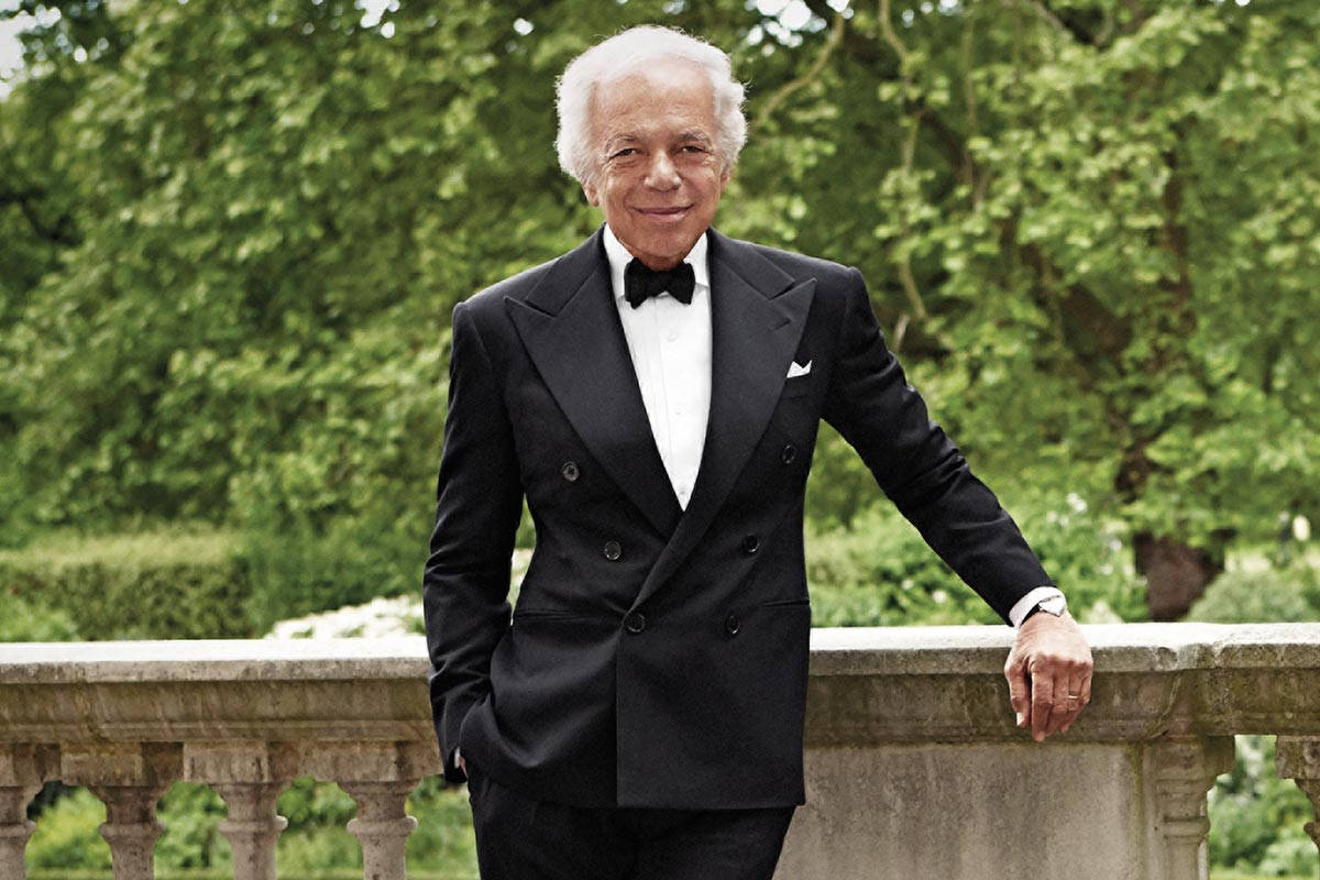 標題：Ralph Lauren 的經典優雅風情 壁紙 — 一位身穿黑色燕尾服、打著領結的長者，倚靠在石欄杆上，背景是翠綠茂盛的花園，面露微笑。
