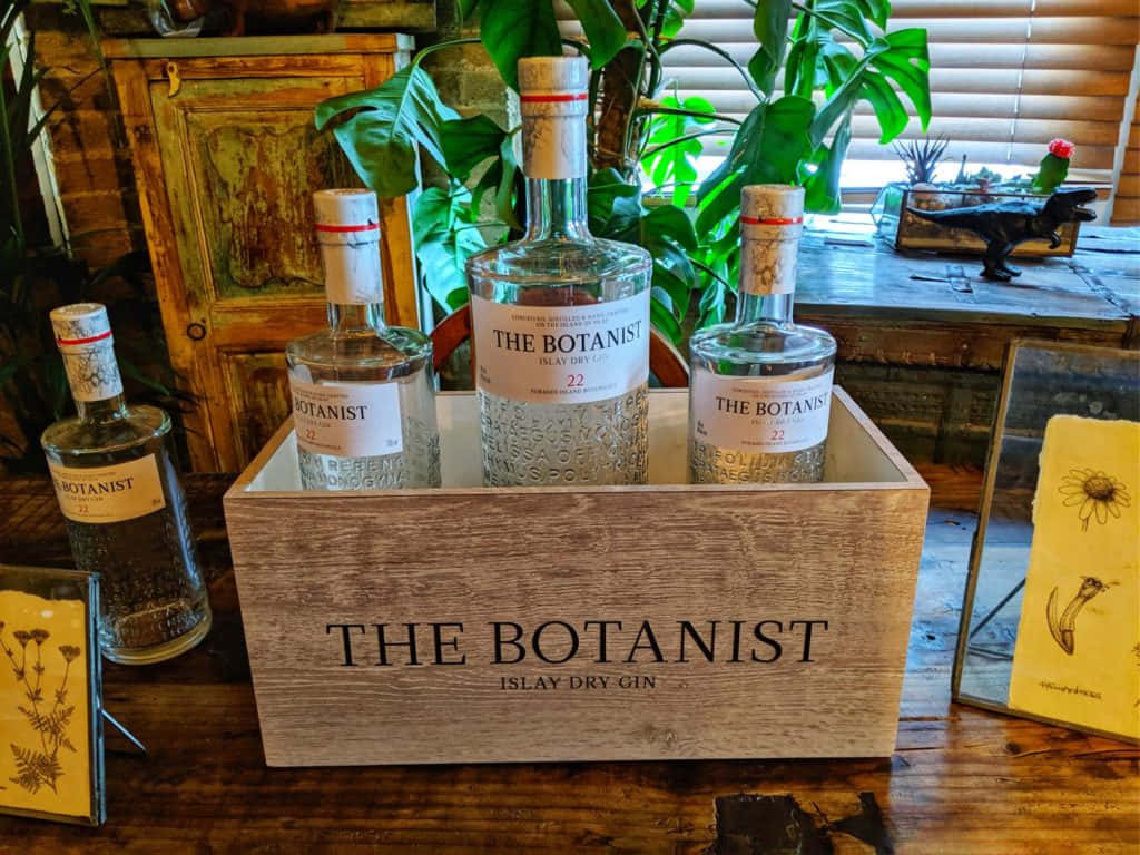 四瓶 The Botanist 琴酒放在木箱中，置於一張有植物和復古物品的木桌上。
