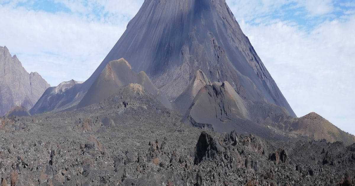 一座大型火山山脈，擁有深色山坡和多岩石的地形，天空多雲。