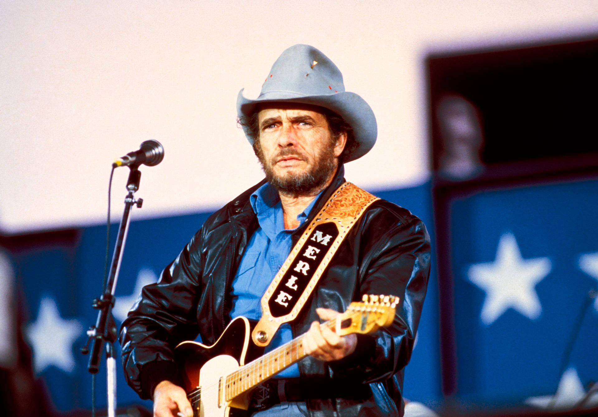 Merle Haggard 在星空背景的舞台上彈結他。