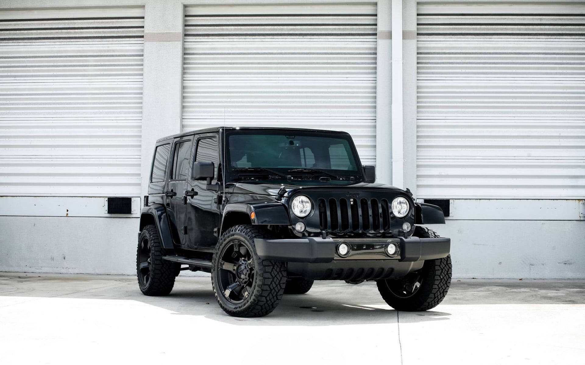 黑色Jeep Wrangler停泊在白色車庫門前的混凝土上。