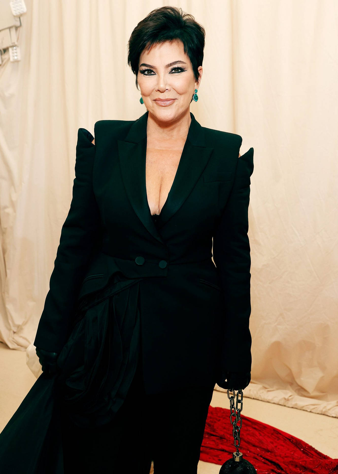 Kris Jenner 喺正式活動中身穿帶有荷葉邊肩部同鏈條手袋嘅黑色西裝外套。
