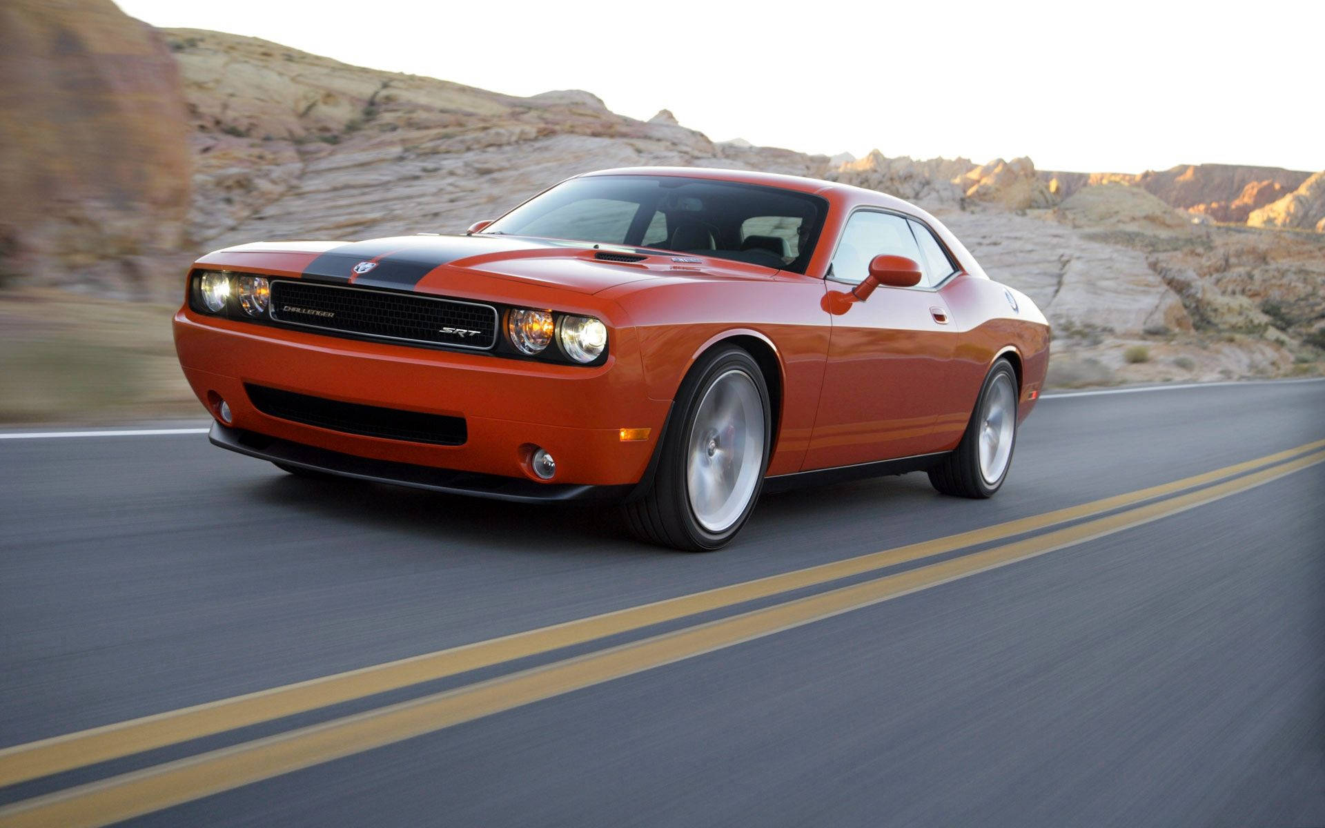 橙色 Dodge Challenger 在日落時分的沙漠公路上疾馳。