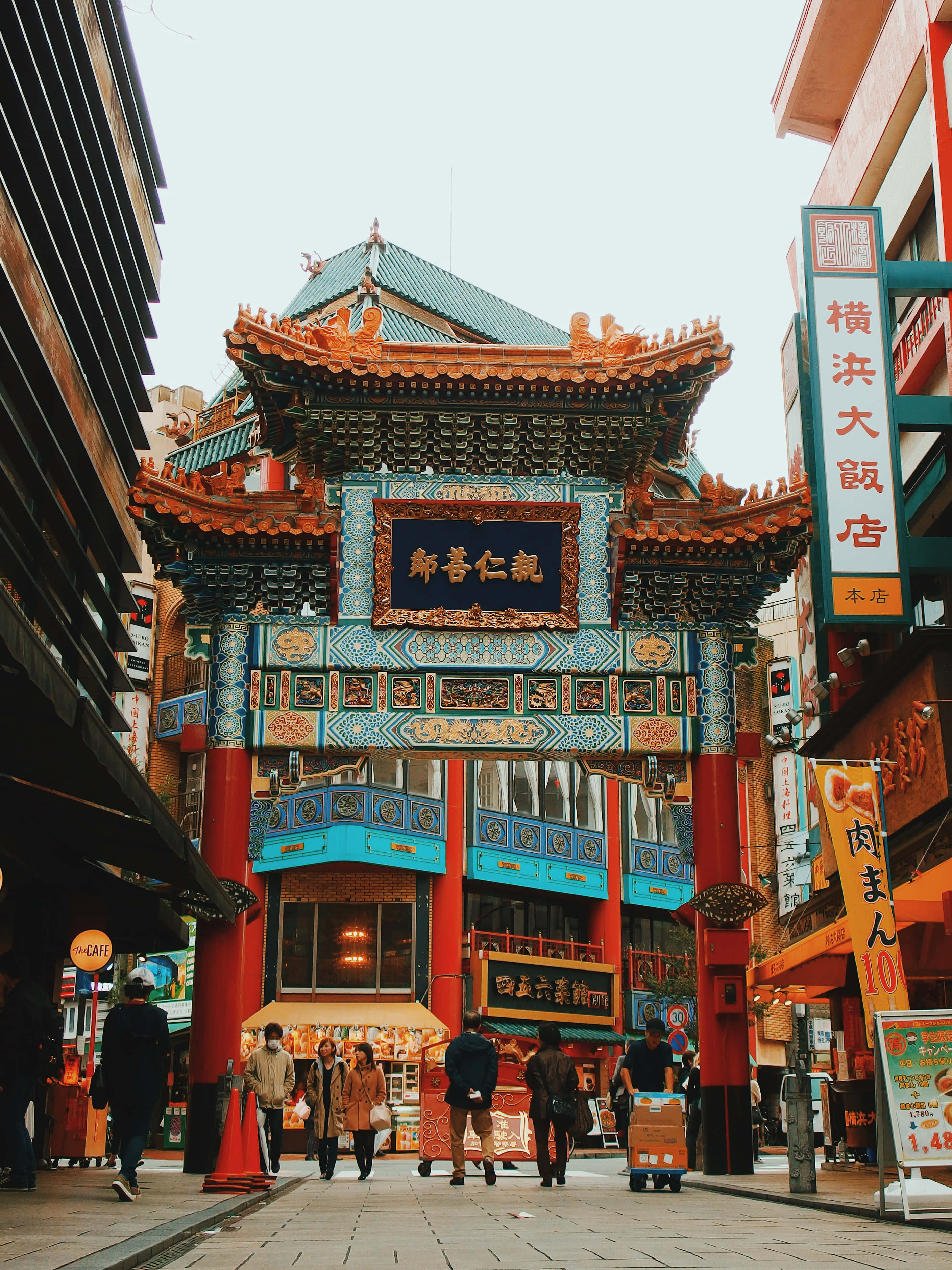 標題：夜間傳統中國燈籠 壁紙 — 一座充滿活力的傳統中式大門，帶有華麗的藍色和紅色細節，矗立在繁忙的都市街道上，街道上滿是行人和色彩繽紛的招牌。