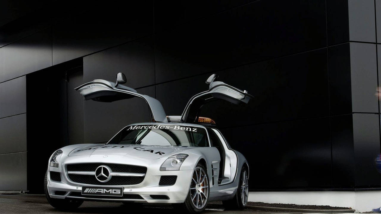 銀色平治 SLS AMG 安全車，鷗翼車門打開，停在黑色建築前。