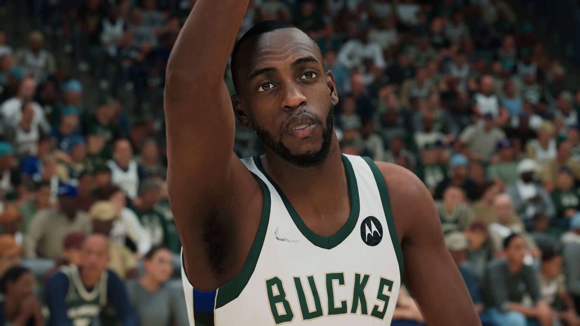 標題：決心滿滿的克里絲·米德爾頓在NBA 2K賽場 壁紙 — 一名身穿密爾沃基公鹿隊球衣的籃球運動員在擠滿觀眾的場館中，對焦舉起手臂，背景人群模糊。