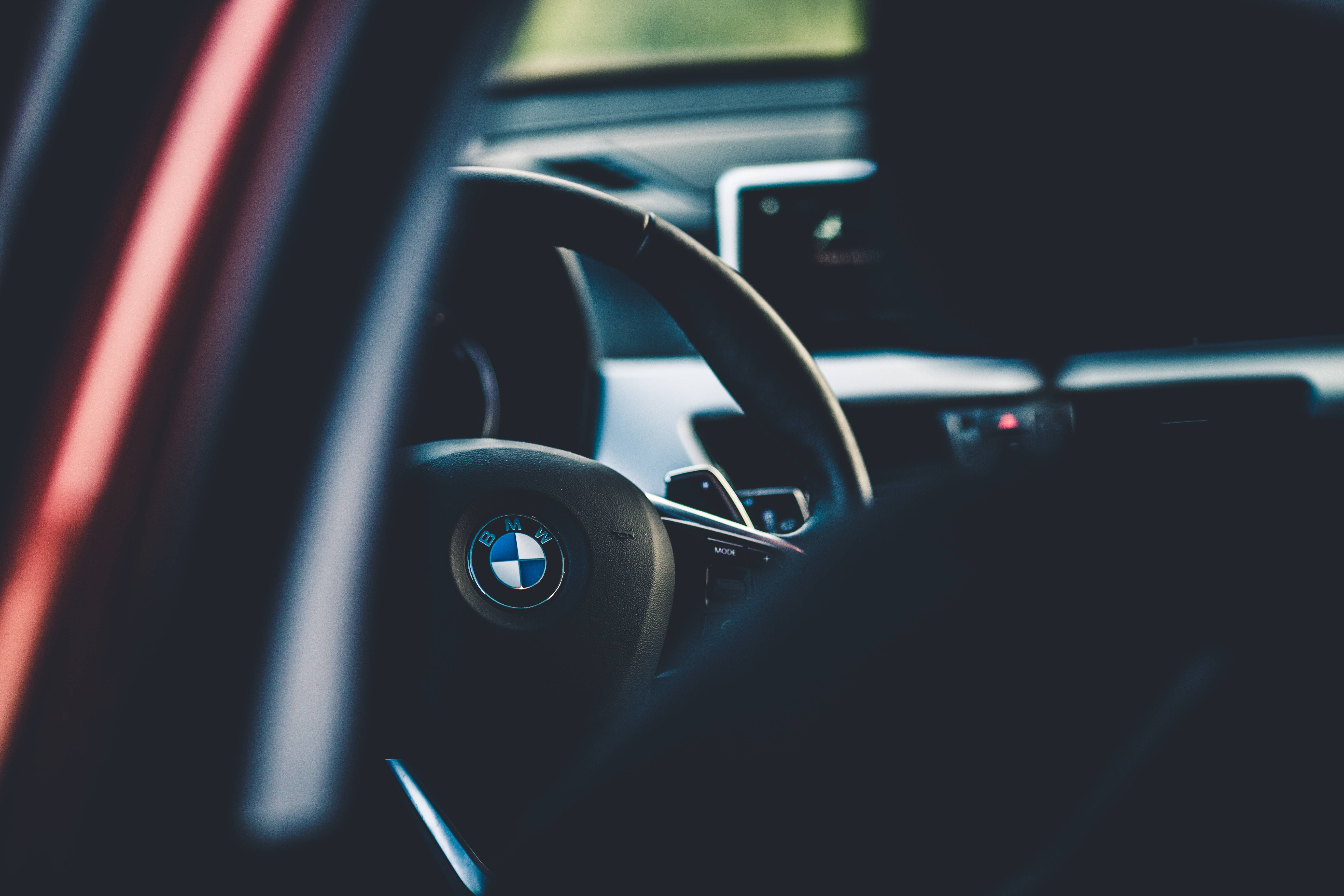 標題：流線型黑色BMW穿梭城市 壁紙 — 寶馬車內方向盤的特寫，帶有模糊的儀表板和紅色環境照明。