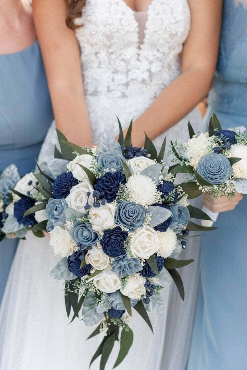 標題：盛開的絢麗藍玫瑰 壁紙 — 一位身穿白色蕾絲婚紗的新娘手持一束由海軍藍和白色玫瑰搭配綠葉組成的瀑布式花束。