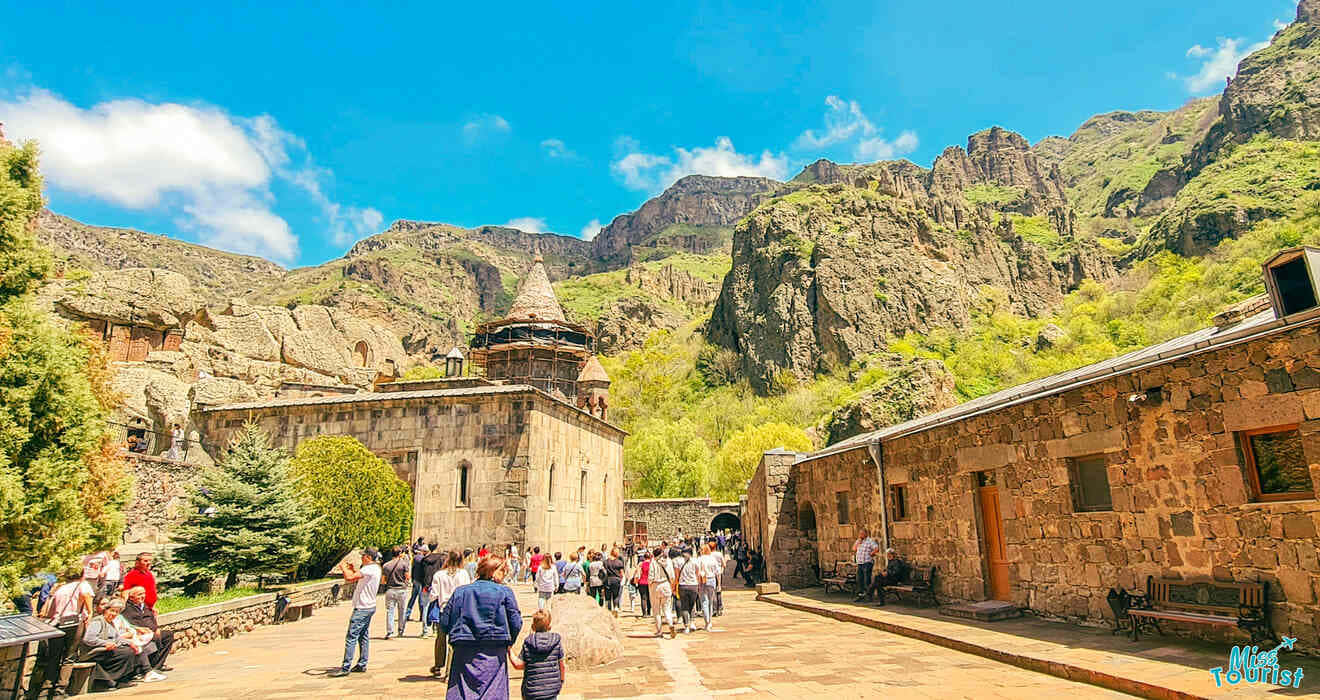 人們在陽光明媚的日子裡參觀位於多山綠色山谷中的歷史石頭修道院。