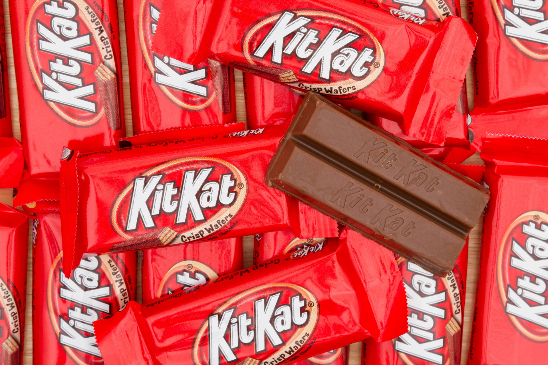 標題：美味的 Kit Kat 巧克力堆疊 壁紙 — 紅色KitKat包裝紙和破碎朱古力棒的近距離特寫，露出脆脆的威化餅。