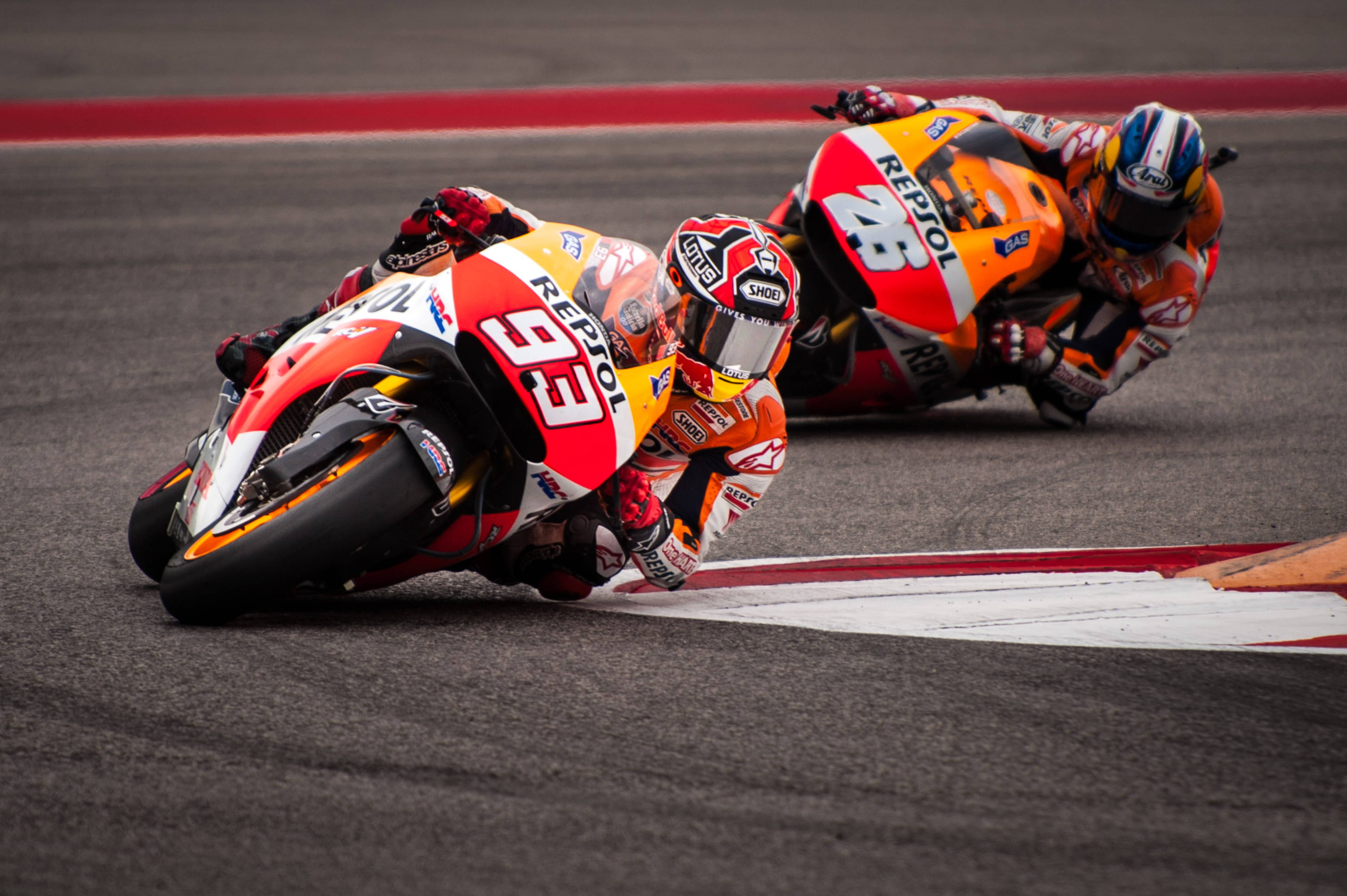 標題：馬奎茲與佩德羅薩的激烈 MotoGP 賽事 壁紙 — 兩名電單車手在陰天下，在設有紅白路緣石的賽道上急劇傾斜入彎。