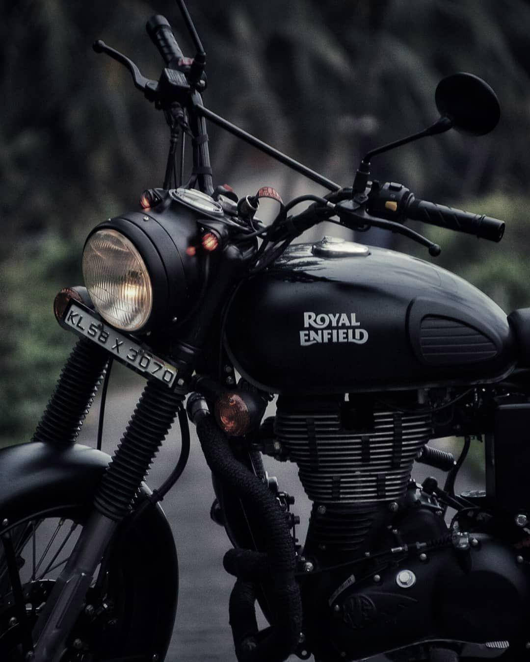 標題：高畫質皇家恩菲德，氣勢磅礡 壁紙 — 一架時尚的黑色 Royal Enfield 電單車，車頭燈亮著，停在公路上，背景是模糊的森林。