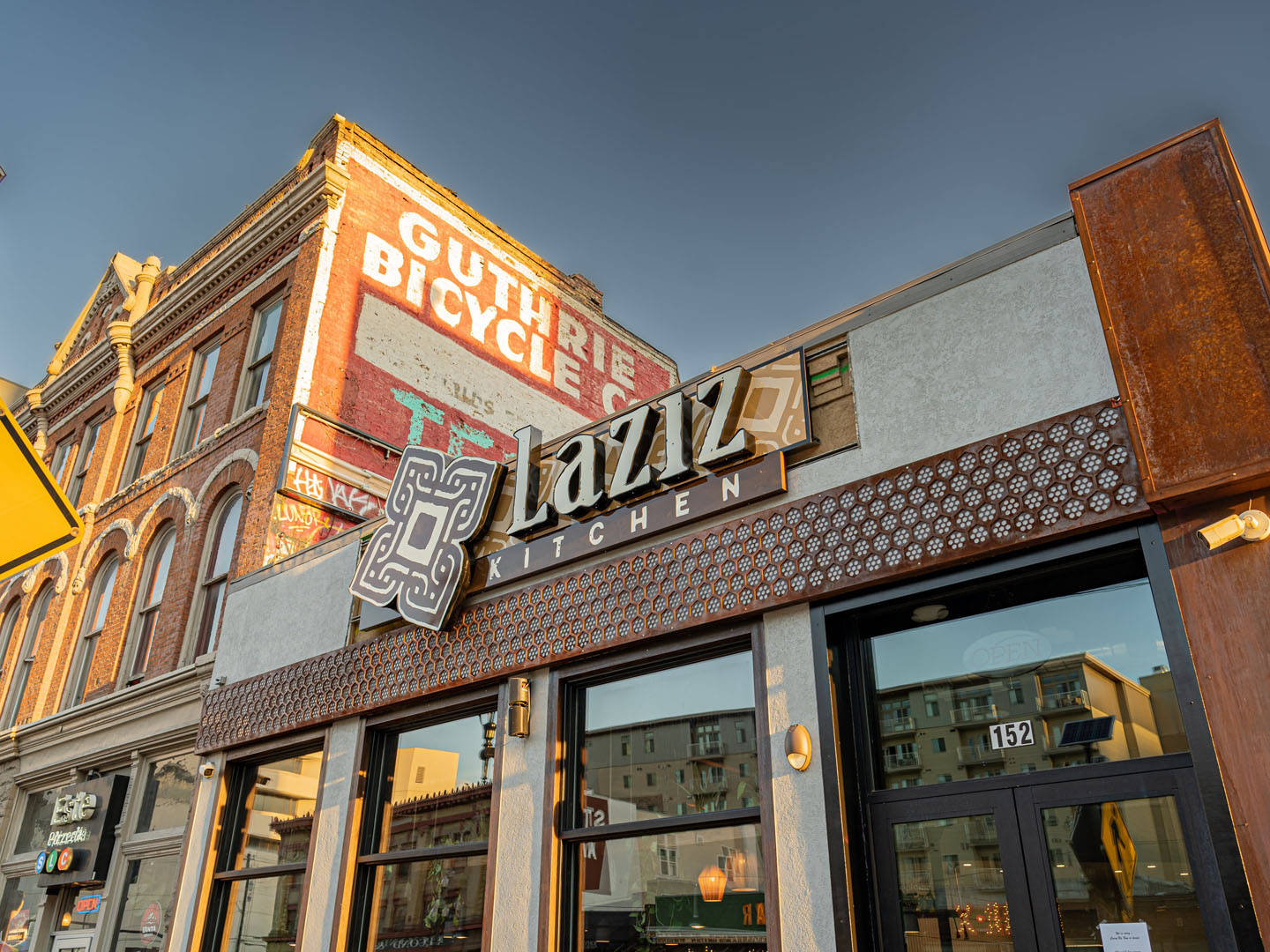 Laziz Kitchen餐廳，相鄰的磚砌建築上有復古Guthrie Bicycle Co標誌，日落時分。