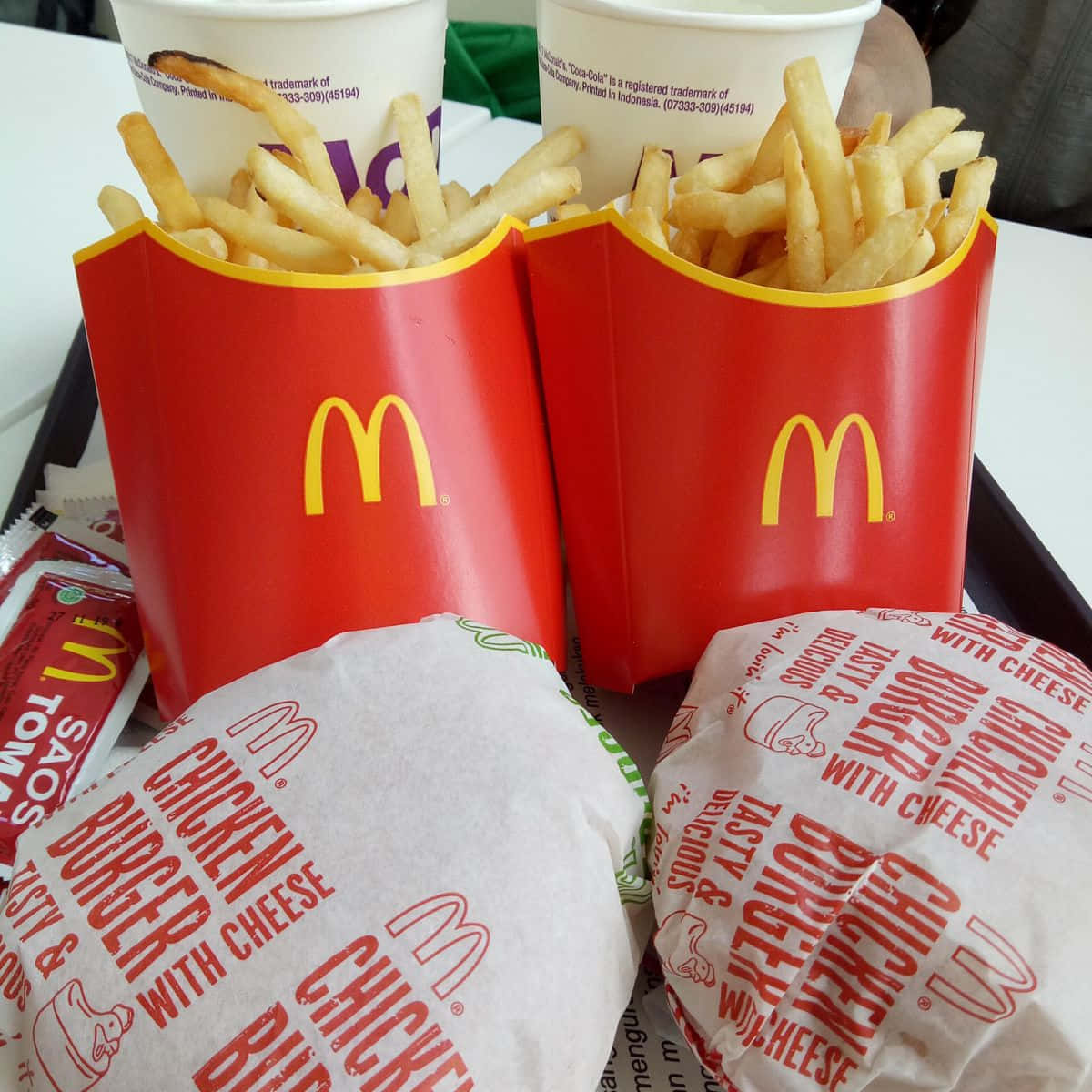 標題：麥當勞經典美食的美味拼盤 壁紙 — 兩個紅色麥當勞薯條盒和包裝雞肉漢堡放在托盤上，附有醬料包和飲料。