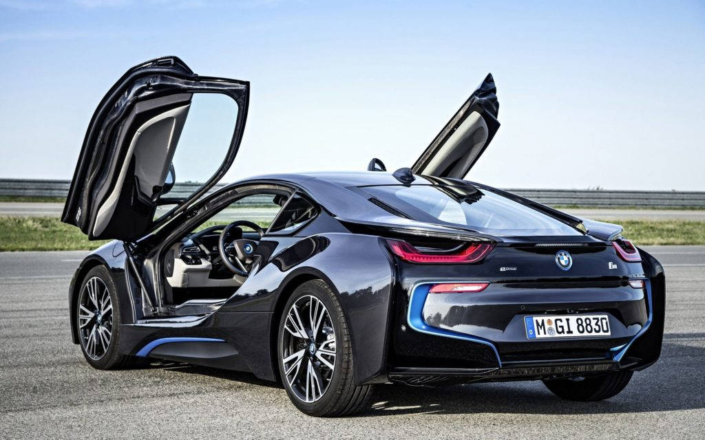 標題：黑色BMW盡顯榮耀 壁紙 — 一架流線型黑色BMW i8跑車，在晴朗藍天下於賽道上打開鷗翼車門。
