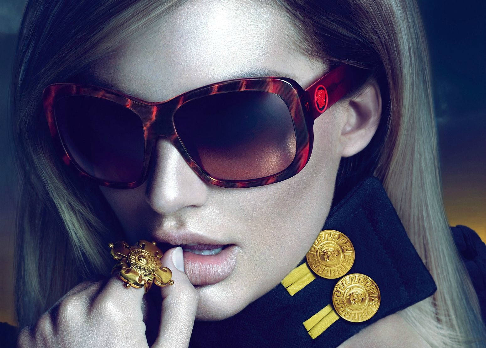 模特兒 Candice Swanepoel 戴 Versace 太陽眼鏡 壁紙 — 一位迷人女性戴著大膽的紅色玳瑁太陽眼鏡和金色珠寶，背景是模糊的深色。