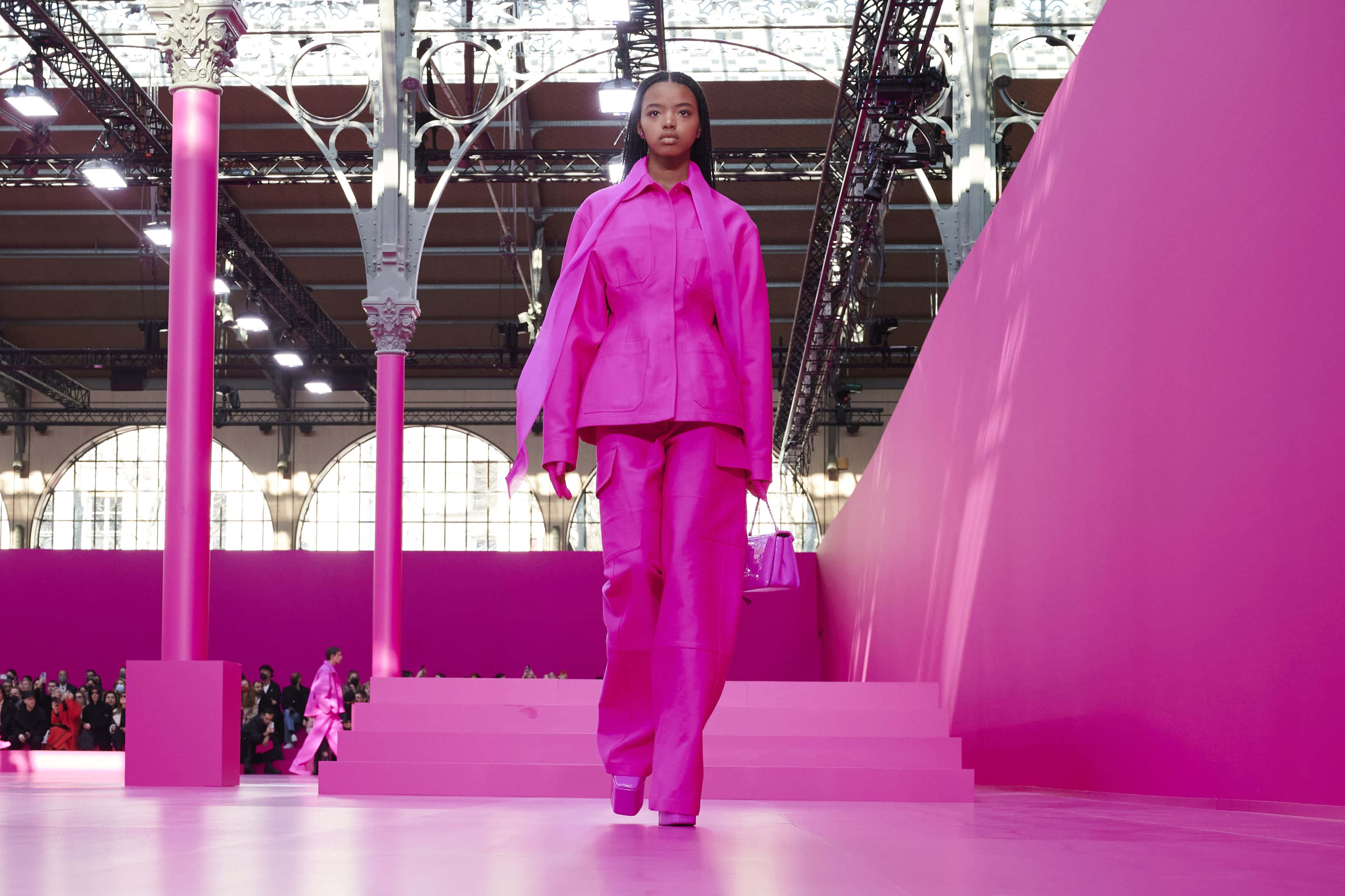 Pink Fashion 桌布 壁紙 — 模特兒喺工業風格嘅玻璃天花下，自信咁行喺充滿活力粉紅色嘅天橋上。